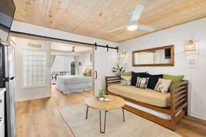 Una habitación acogedora con techo de madera, un sofá, una mesita y una cama al fondo.