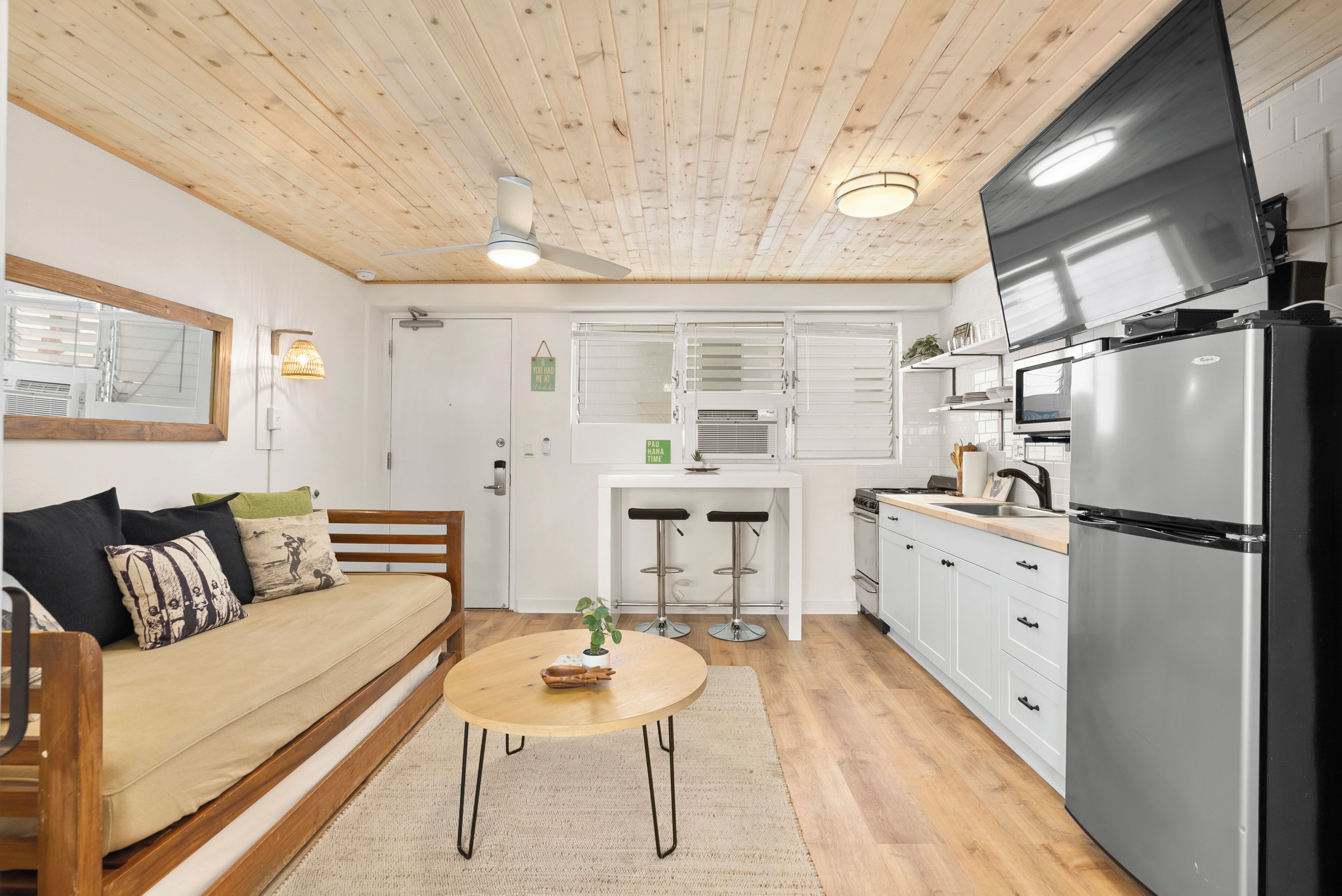 Eine kompakte Küche mit Holzboden, ein Essbereich mit rundem Tisch und ein Sofa mit Kissen.
