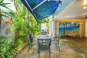 Un patio cubierto con una mesa y sillas, rodeado de exuberante follaje y un mural de playa.
