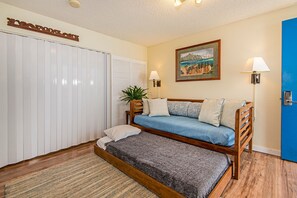 Ein Schlafzimmer mit einem hölzernen Bett, einem blauen Sofa, einem weißen Kleiderschrank, einem gerahmten Bild an der Wand und zwei Wandleuchten.