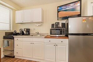 A kitchen with white cabinets, a stainless steel refrigerator, a microwave, a stove, and a window with blinds. - Family Vacation Condo W/full Kitchen by the Beach & Near Shops & Restaurants (Honolulu)