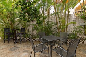 Eine Terrasse im Freien mit Tisch und Stühlen, umgeben von üppigem Grün und einem dekorativen Zaun.