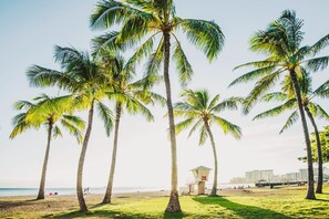 A beach with palm trees, a lifeguard tower, and a cityscape in the background. - Family Vacation Condo W/full Kitchen by the Beach & Near Shops & Restaurants (Honolulu)