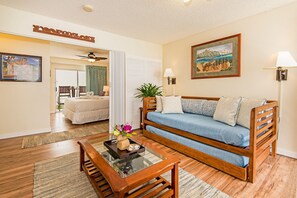 A living room with a wooden sofa, a glass coffee table, and a painting on the wall. - Family Vacation Condo W/full Kitchen by the Beach & Near Shops & Restaurants (Honolulu)