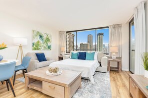 A modern hotel room with a city view, a large bed, a sofa, a desk, and a dining area. - Ocean & City Views Renovated Condo at Aloha Towers W/washer-dryer & Parking (Honolulu)