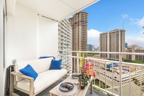 A balcony with a white sofa, a dining table set with plates, a bottle, and a vase with flowers. - Ocean & Fireworks Renovated Condo at Ilikai Hotel With Full Kitchen & Wifi (Honolulu)