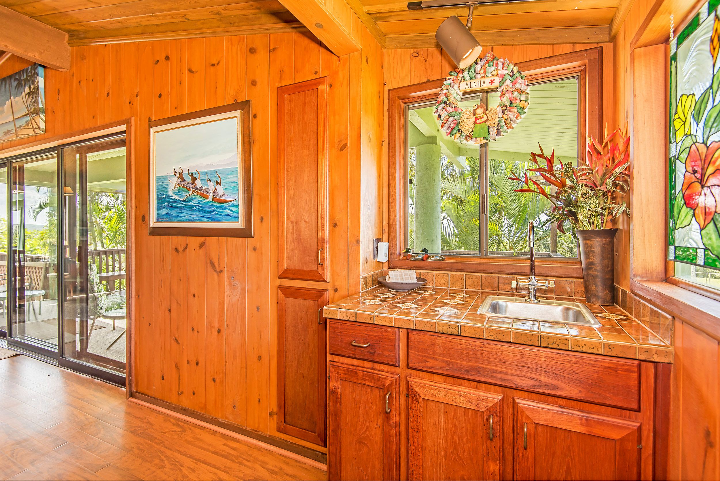 A wooden interior with a kitchen area, a dining area with glass doors, and a painting of a boat on water.