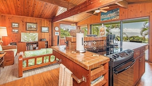 Interior em madeira com cozinha, área de refeições e uma janela ampla que oferece vista para o verde.