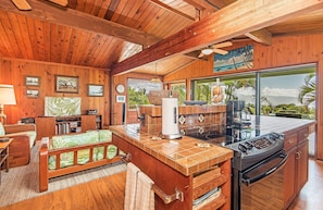 Interior em madeira com cozinha, área de refeições e uma janela ampla que oferece vista para o verde.