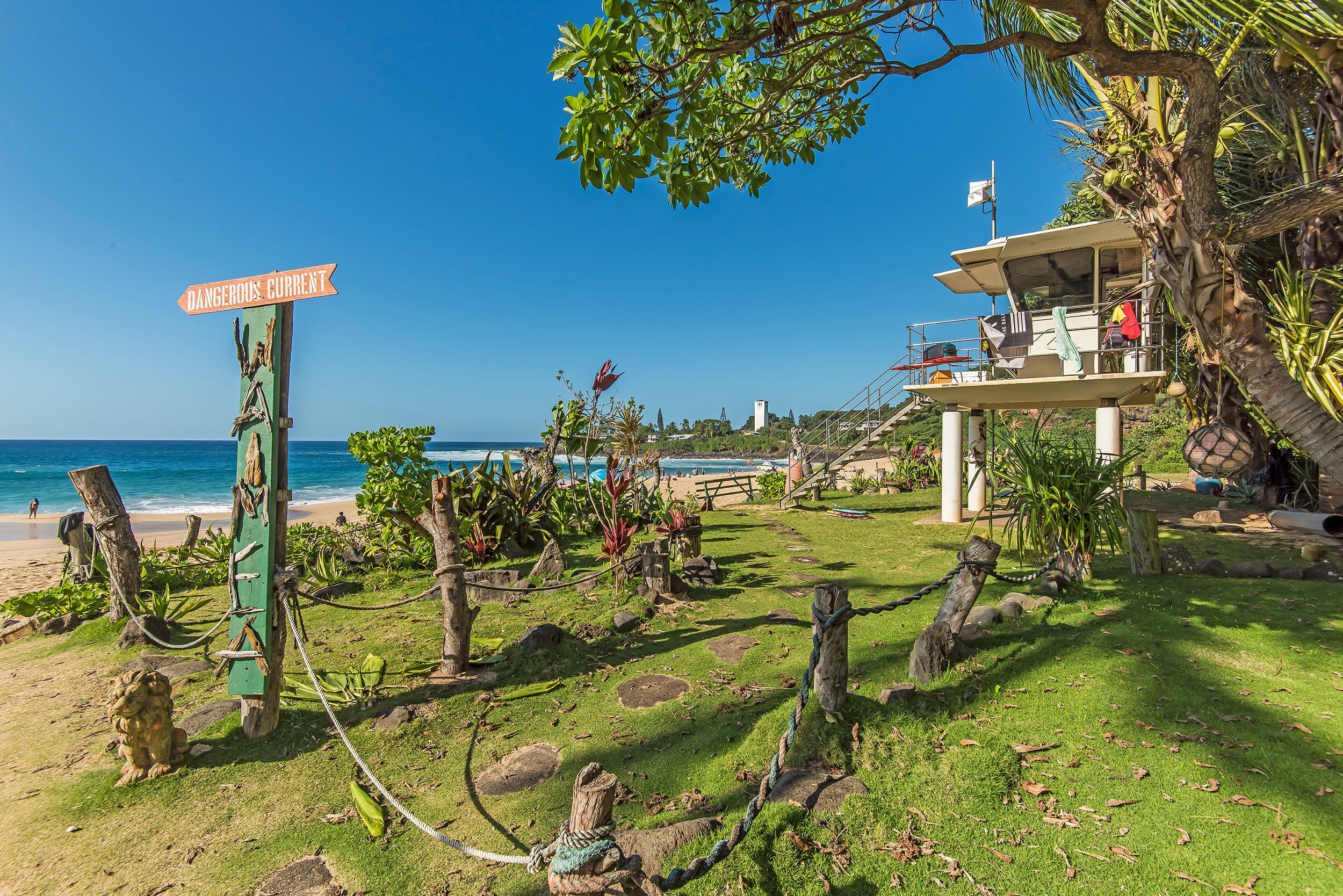 A beach with a lifeguard tower, a sign reading 'DANGEROUS CURRENT,' and a view of the ocean.