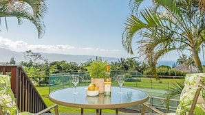 Mesa de vidro redonda com uma garrafa e copos, rodeada por cadeiras com estampa tropical.