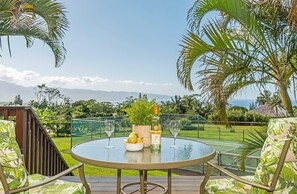 Mesa de vidro redonda com uma garrafa e copos, rodeada por cadeiras com estampa tropical.