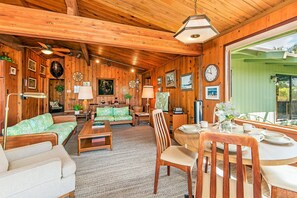 Uma sala de estar acolhedora, com decoração em madeira, um sofá verde, uma mesa de jantar de madeira para quatro pessoas e um ventilador de teto.