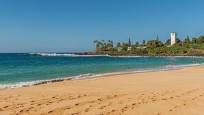 Uma praia com pegadas, céu claro e um edifício com torre.