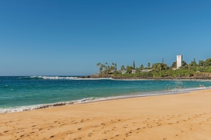 Uma praia com pegadas, céu claro e um edifício com torre.
