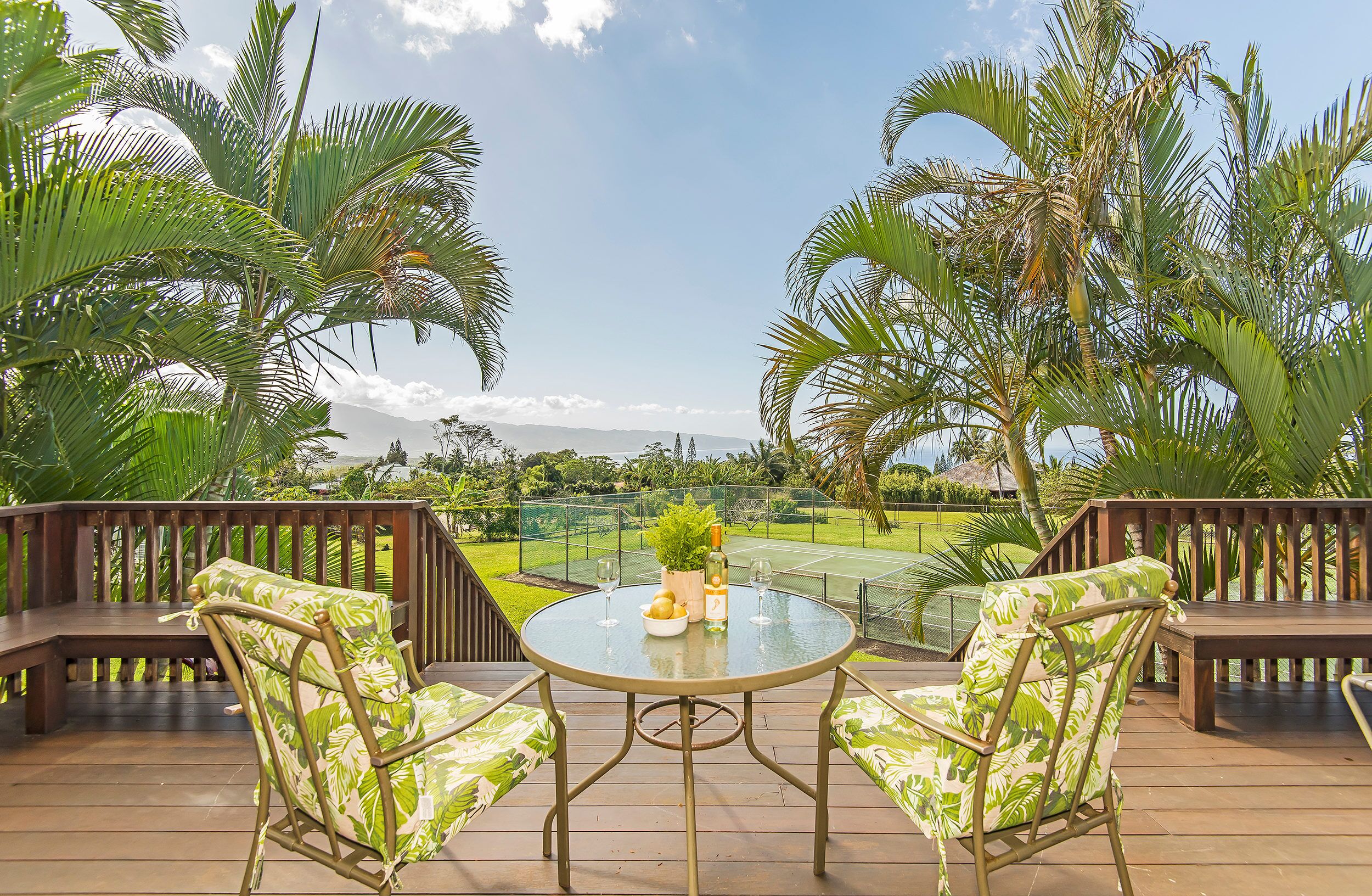 Une terrasse avec deux chaises et une table, offrant une vue sur un court de tennis et une végétation luxuriante.