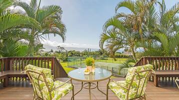 Une terrasse avec deux chaises et une table, offrant une vue sur un court de tennis et une végétation luxuriante.