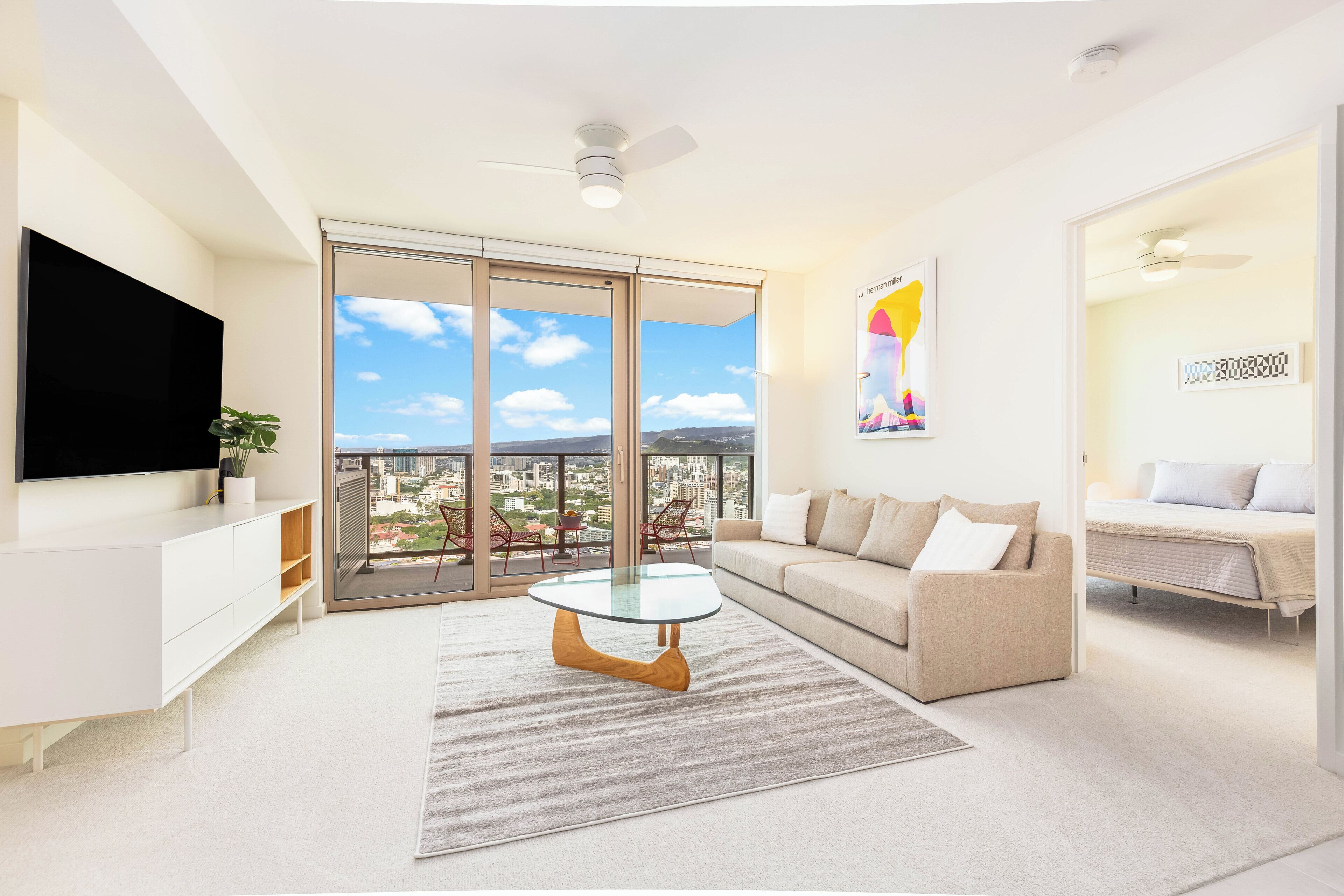 Ein modernes Wohnzimmer mit einem Flachbildfernseher, einem Glastisch, einer Couch und einem Balkon mit Blick auf die Stadt.