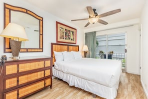 A hotel room with a bed, a wooden dresser, a ceiling fan, a large mirror, and a window with a view. - Steps From the Beach Family Retreat W/free Parking in Boutique Style Building (Honolulu)