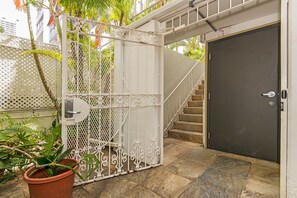 Uma entrada protegida por grades, com um portão de metal, uma porta escura e uma escadaria que leva a um andar superior.