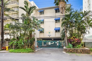A multi-story building with a gated entrance, surrounded by lush greenery and palm trees. - Steps From the Beach Family Retreat W/free Parking in Boutique Style Building (Honolulu)