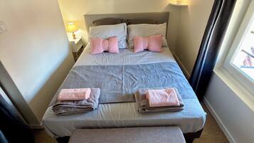 A neatly made bed with pillows and folded towels, a bedside lamp, and a framed picture on the wall.