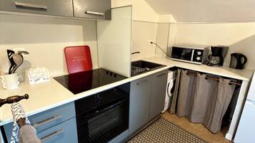 Een kleine keuken met een magnetron, koffiezetapparaat en een rode stoel.