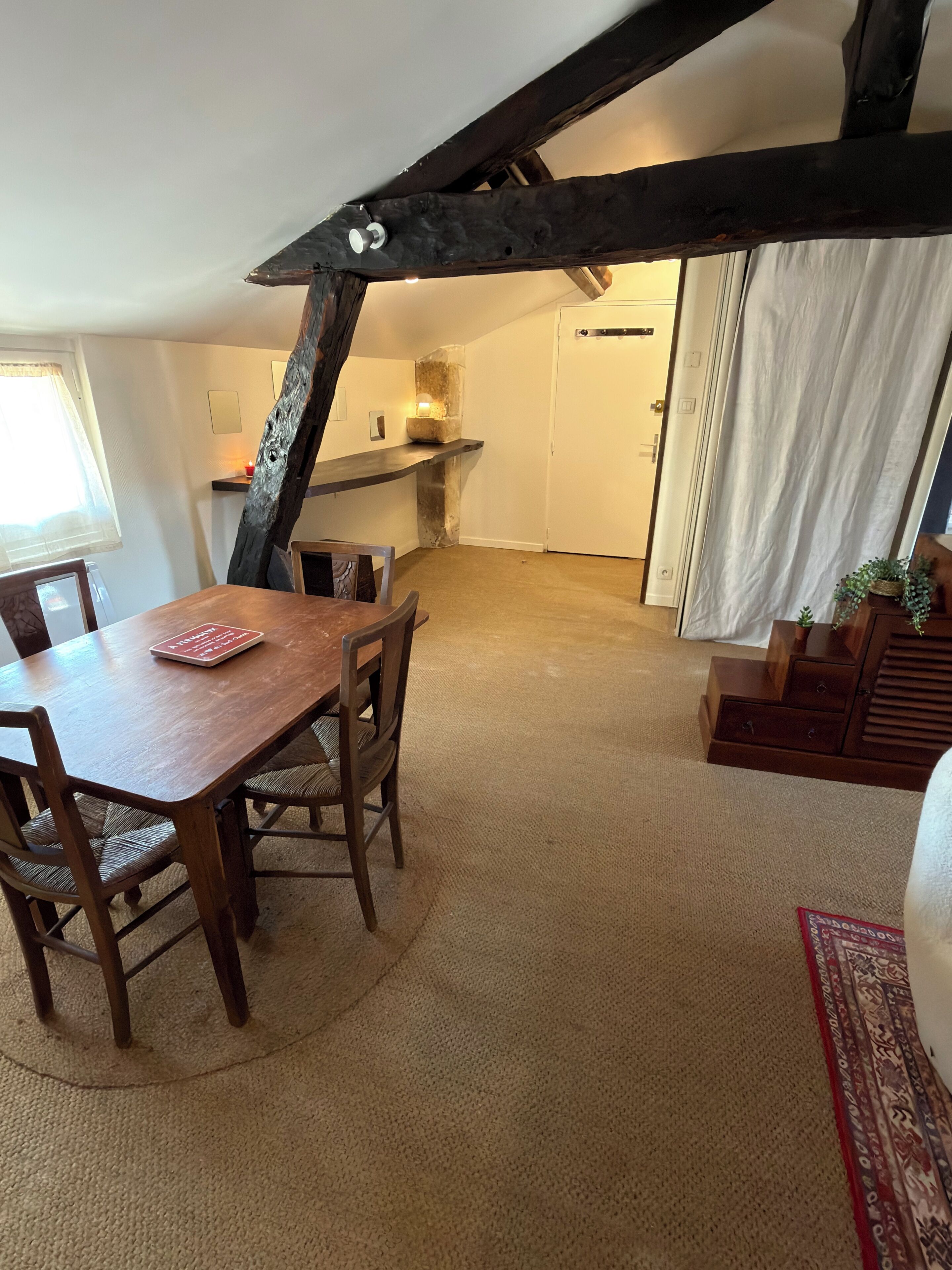 A dining area with a wooden table and chairs, a stone fireplace, and a view of a kitchen and living space.