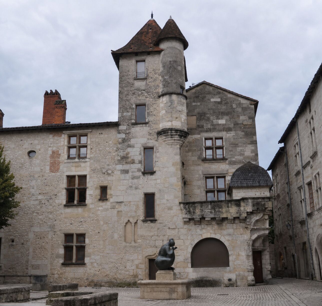 Un edificio de piedra histórico con una torre, ventanas arqueadas y una estatua en el patio.