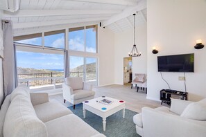 A spacious living room with a large window overlooking a scenic view, a comfortable sofa, a coffee table, and a flat-screen TV.
