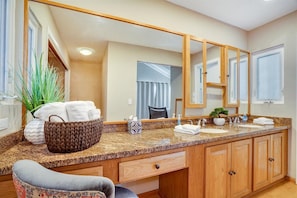 A bathroom with a granite countertop, wooden cabinets, a large mirror, a towel rack, and a potted plant.