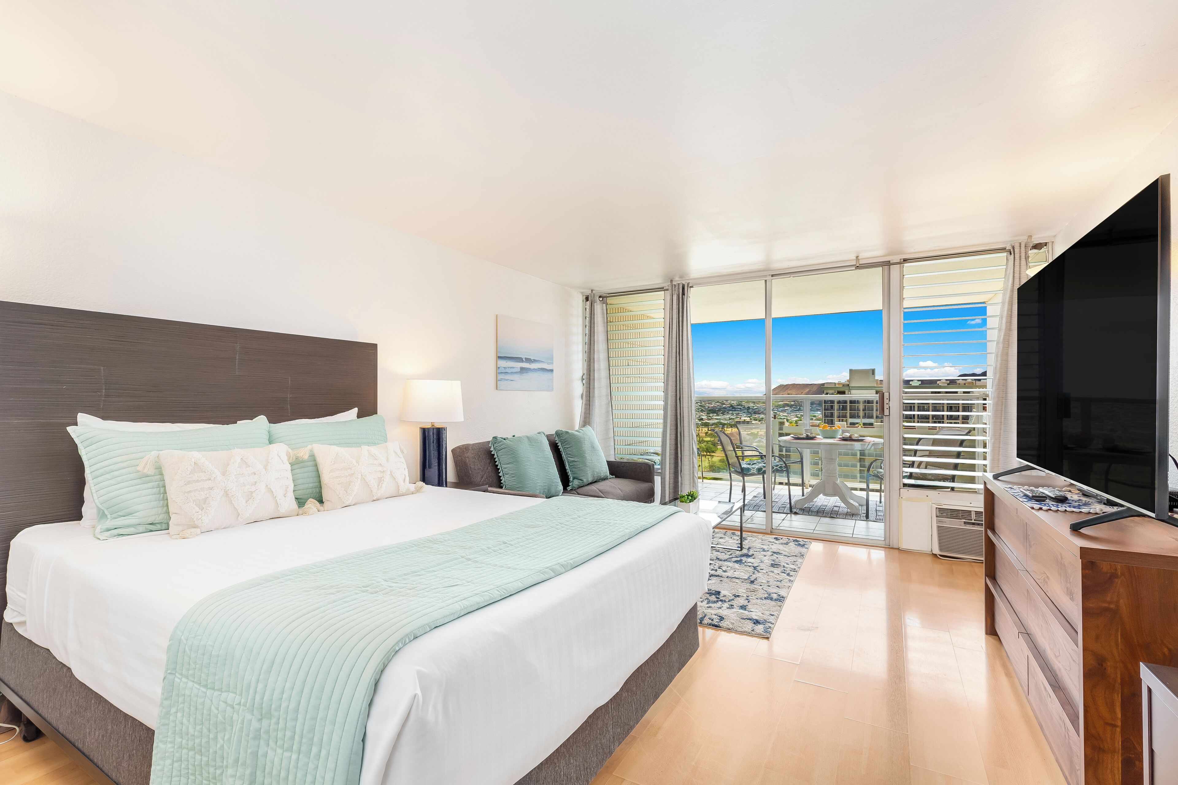 Une chambre d’hôtel moderne dotée d’un grand lit, d’une télévision à écran plat, d’un balcon avec vue sur la ville et d’un coin repas.