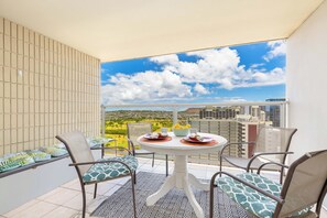 Un balcon avec une table dressée pour deux personnes, des chaises et une vue sur le paysage urbain.
