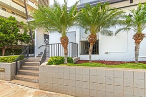 Ein Gebäude mit weißer Fassade, einer Treppe, die zu einem Eingang führt, und Palmen davor.