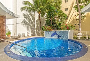 Ein Pool mit Delfin-Mosaik, umgeben von Palmen und Liegestühlen, was auf eine luxuriöse Ferienanlage hindeutet.