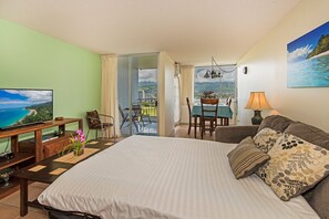 Ein Hotelzimmer mit Bett, Schreibtisch mit Fernseher, Essbereich mit Tisch und Stühlen sowie einem Balkon mit Meerblick.