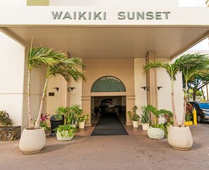 Der Eingang zum Waikiki Sunset mit einem überdachten Gang, Kübelpflanzen und freiem Blick ins Innere des Gebäudes.