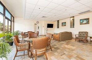 Een ruime lobby met een ronde tafel, rieten stoelen, een bank en potplanten.