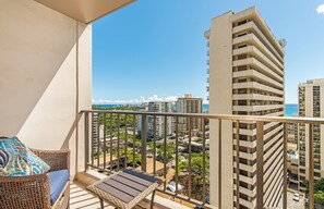 Een balkon met rieten meubilair, uitzicht op de oceaan en hoge gebouwen op de achtergrond.