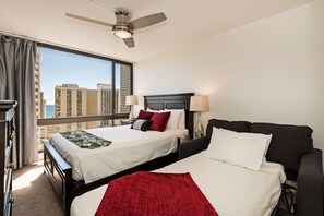 Ein Hotelzimmer mit zwei Betten, einem Deckenventilator und einem großen Fenster mit Blick auf die Stadt.