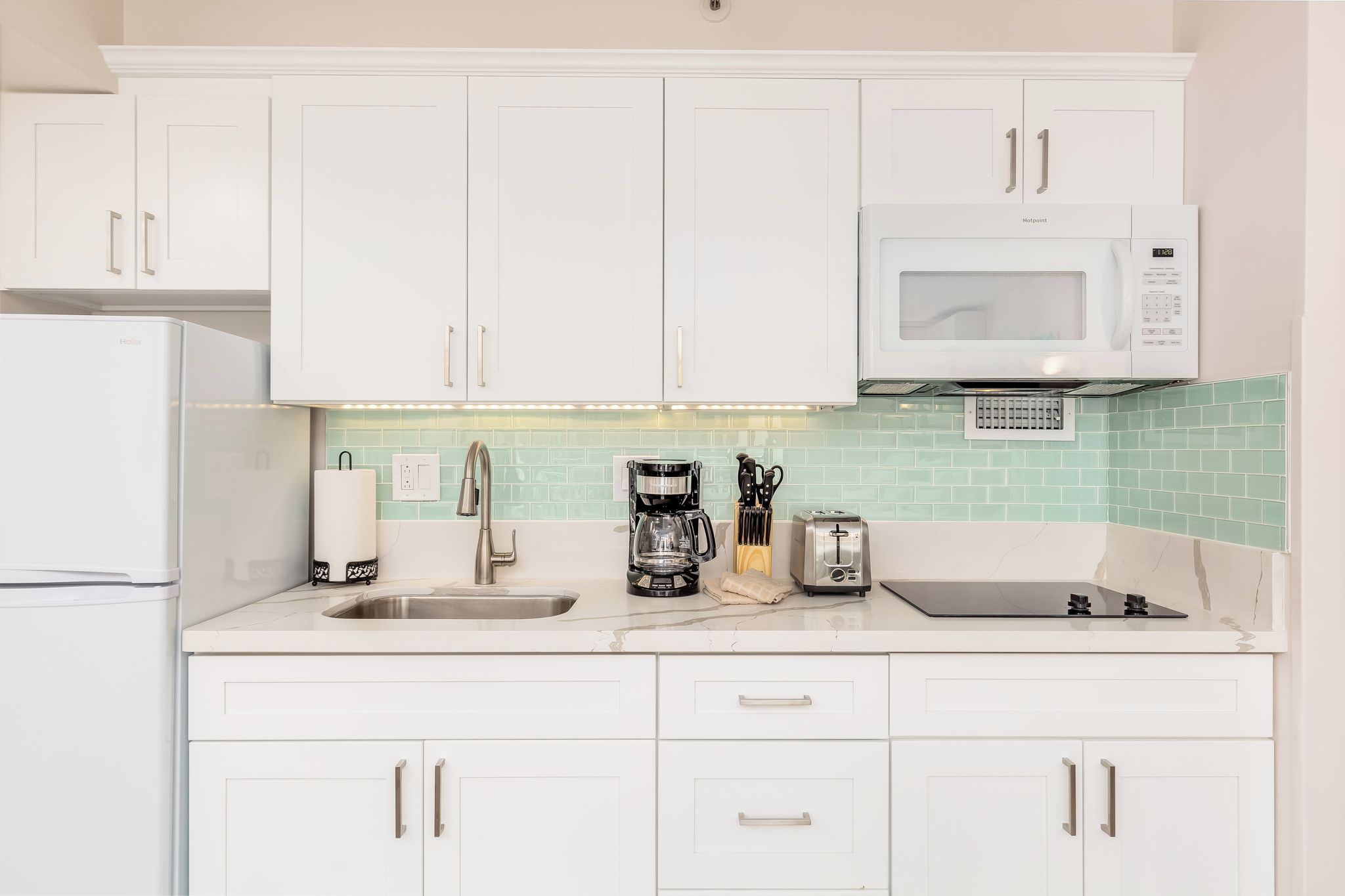 A kitchen with white cabinets, a microwave, a coffee maker, and a toaster.