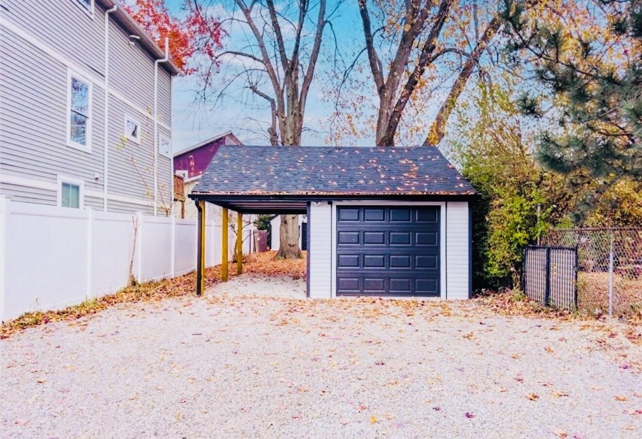 Garagem residencial com calçada de cascalho, garagem coberta e uma casa ao fundo.