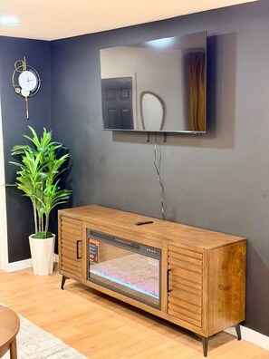 A modern living room with a wooden cabinet, a flat-screen TV mounted on the wall, a wall clock, and a potted plant. - Modern Home in the vibrant Ohio city neighborhood (Cleveland)
