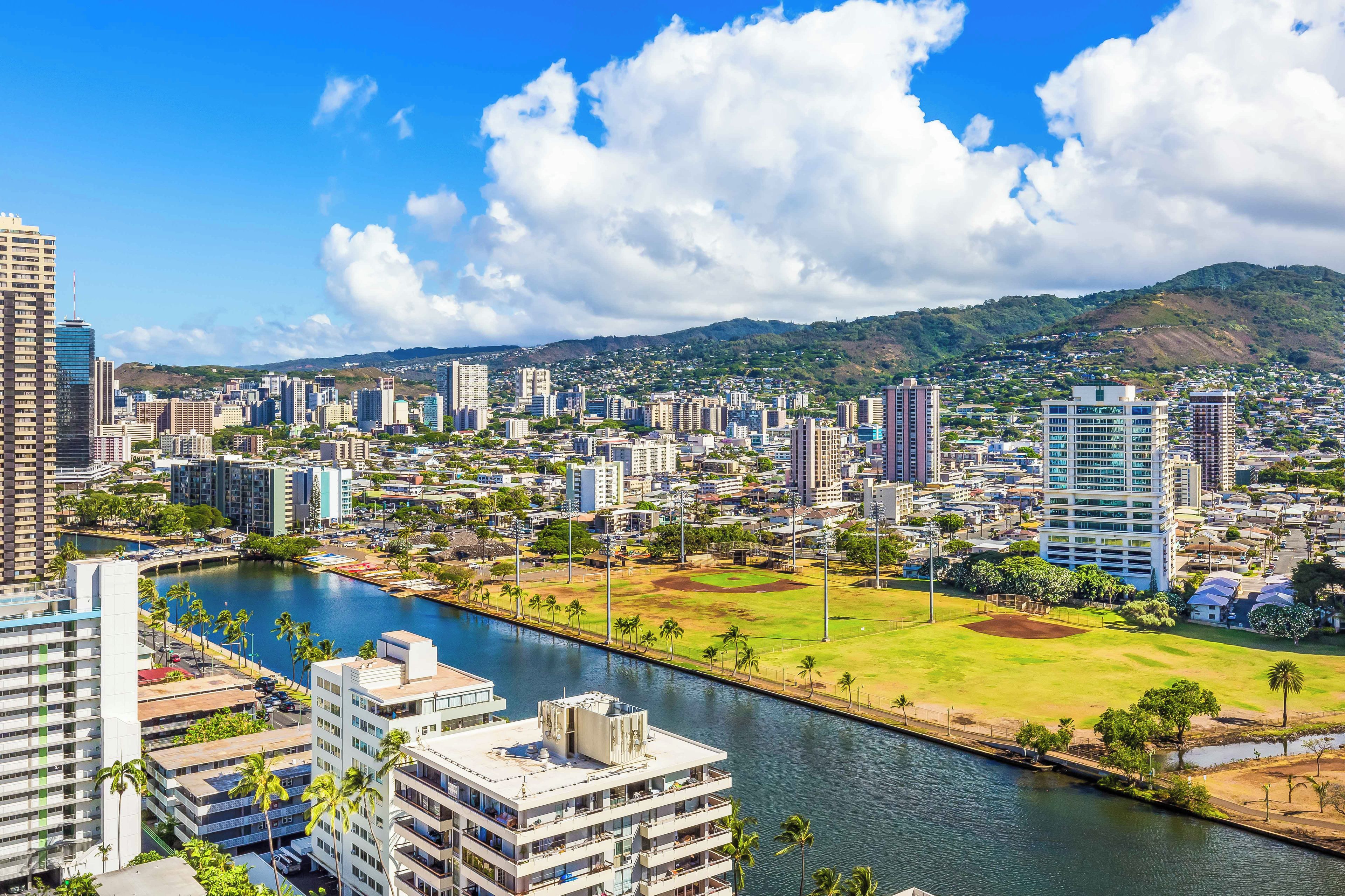 A cityscape with a river, buildings, and a hilly background.