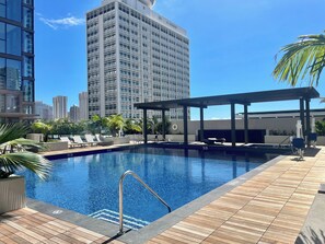 A rooftop pool with a wooden deck, lounge chairs, and a city skyline in the background. - Ocean-city Luxurious Vacation at the Sky Ala Moana With Amazing Amenities (Honolulu)