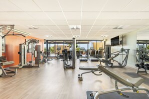 A gym with various exercise equipment, large windows, and a wooden floor. - Ocean View Paradise Escape at Waikiki Beach Tower Near Shops & Restaurants (Honolulu)