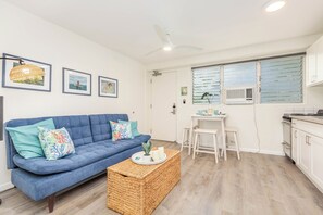 Ein modernes Wohnzimmer mit einem blauen Sofa, einem Korpus-Couchtisch und einem Essbereich mit einem weißen Tisch und Stühlen.