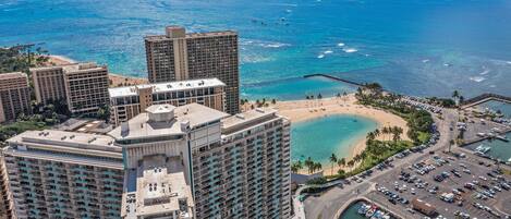 A high-rise hotel with multiple floors, a marina with boats, and a beach with palm trees.