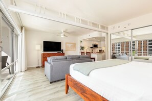 A hotel room with a bed, a sofa, a television, a ceiling fan, and a view of the cityscape through large windows. - Ocean & Fireworks Views Condo at the Ilikai Hotel W/full Kitchen & Free Wifi (Honolulu)