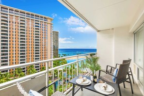 A balcony with a table set for two, overlooking a beach and a pool area with palm trees. - Ocean & Fireworks Views Condo at the Ilikai Hotel W/full Kitchen & Free Wifi (Honolulu)